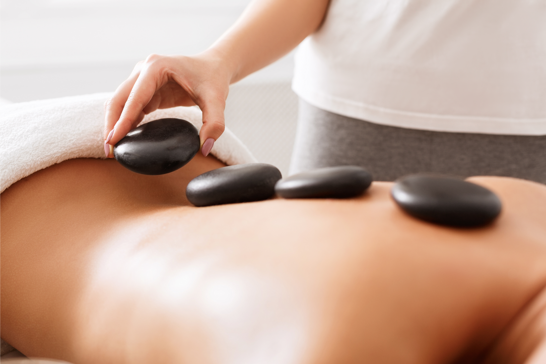 Masseuse doing hot stones massage to female client, placing stones on back, closeup