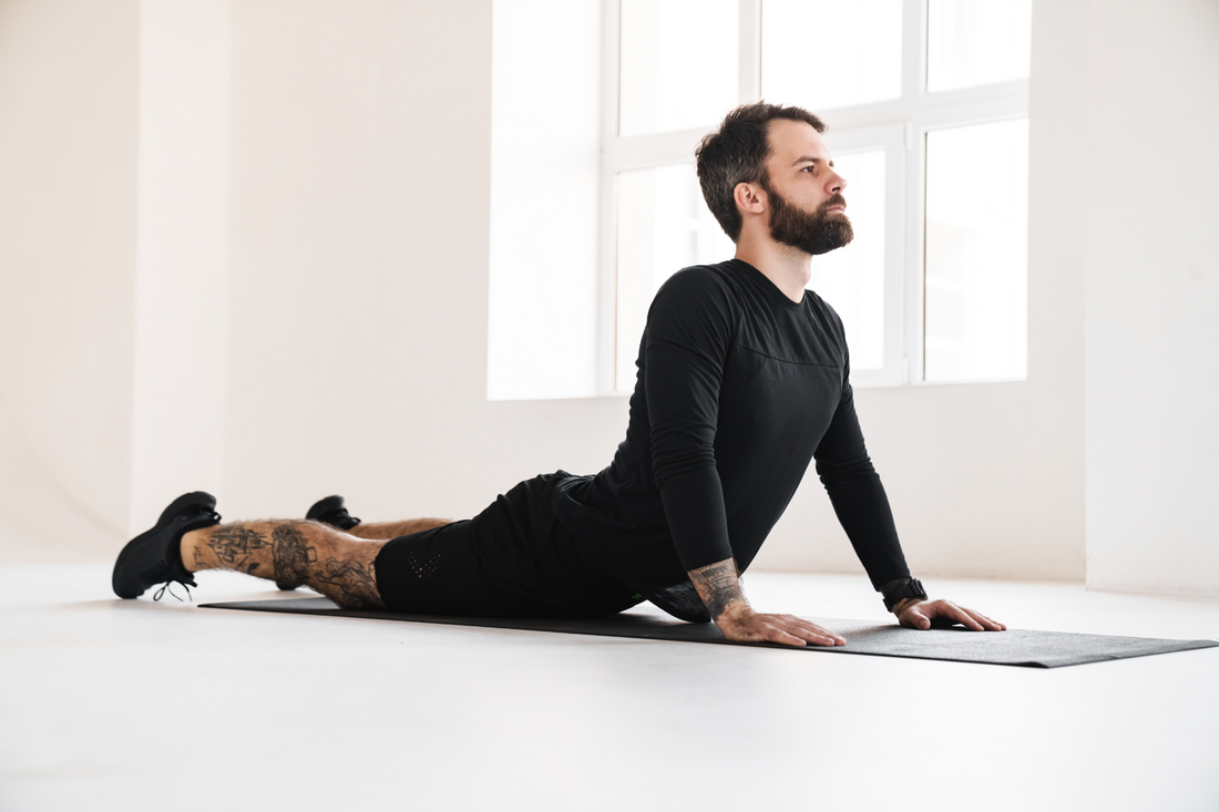 Young brunette bearded man in sportswear stretching while laying on a fitness mat indoors