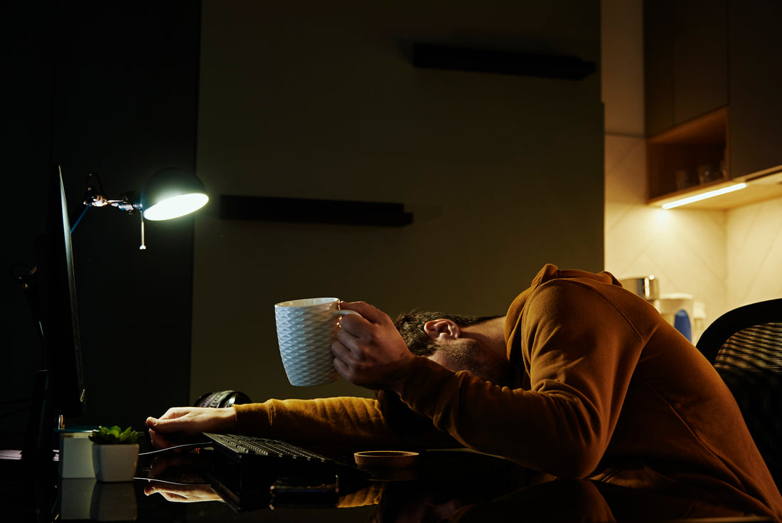 Man sleeping at home office workplace with cup of coffeee in his hand. Freelancer remotely working late. Emotional stress and burnout